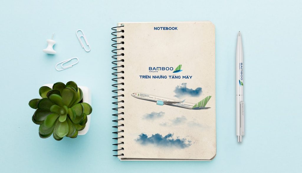 Notebook dengan tema pesawat dan bambu, pen, dan tanaman hias.