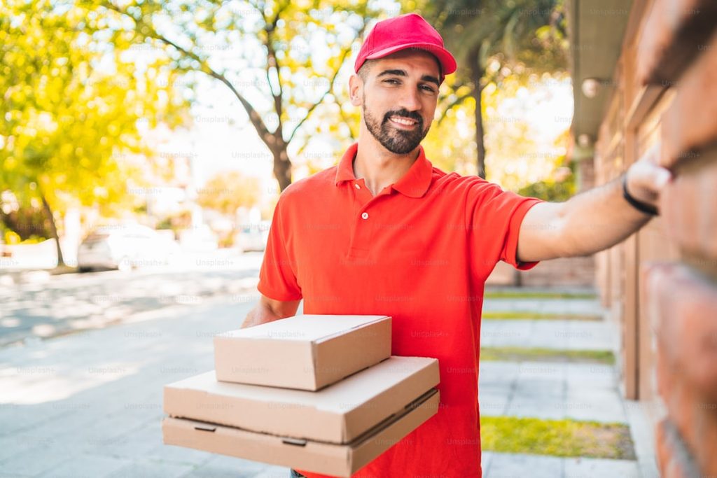 Pria pengirim makanan merah menyerahkan kotak pizza dan kemasan kecil.