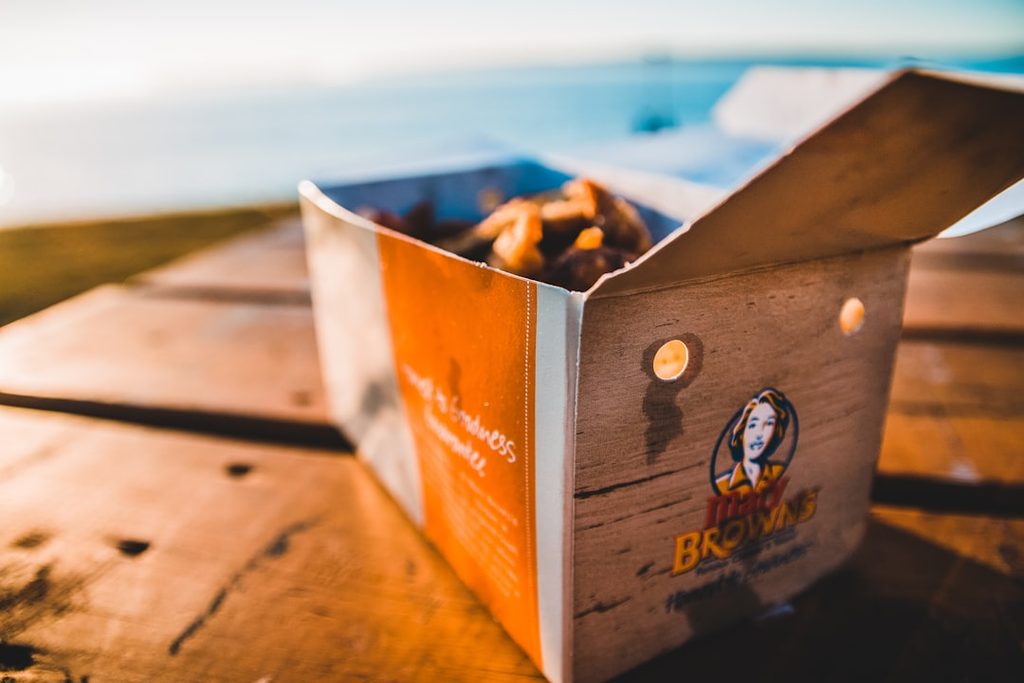 Kotak brownies dari Uprint.id di meja kayu, latar belakang pantai.