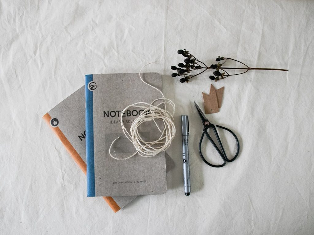 Buku catatan, tali, pensil, gunting, dan kertas di atas latar putih.