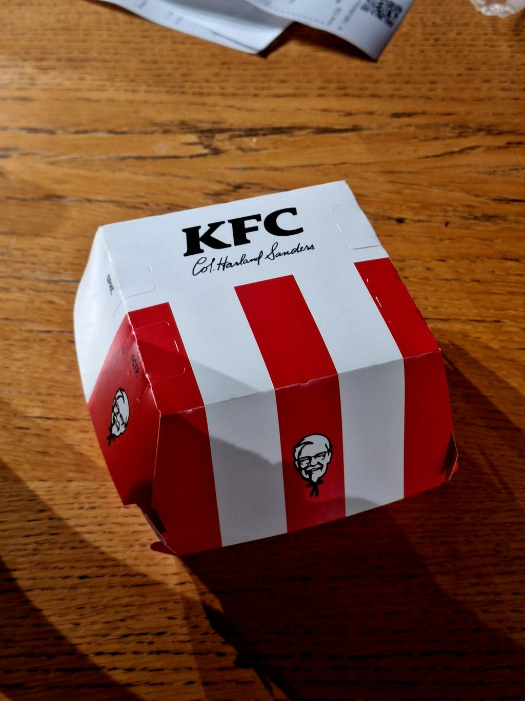Kotak makanan KFC dengan garis merah putih dan logo KFC sebagai contoh branding ikonik