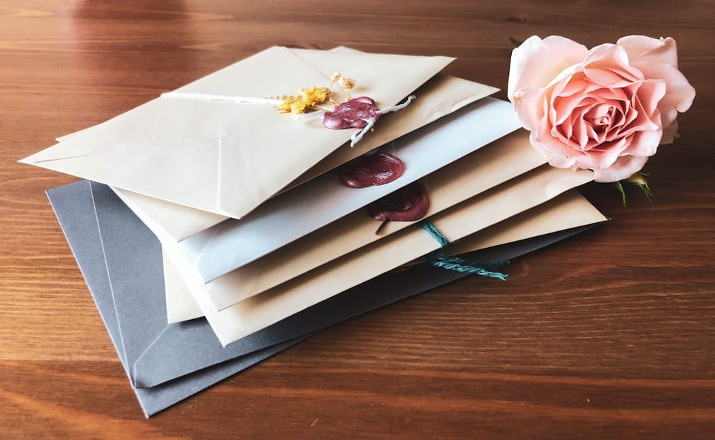 Stack of envelopes with a rose and wax seal, perfect for wedding invitations or special occasions.