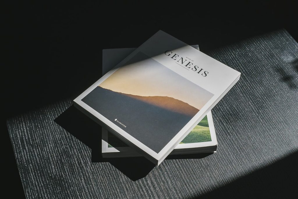 Buku Genesis dengan cover berwarna biru dan hijau, diletakkan di atas meja.