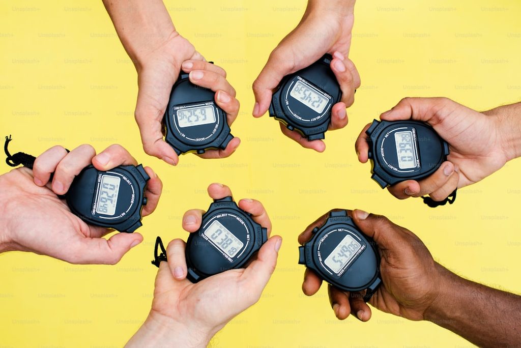 Empat tangan memegang stopwatch yang menggambarkan pentingnya timing dan sinkronisasi branding offline dan online.