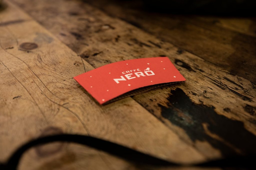 Brosur merah dengan logo Caffe Nero di atas meja kayu.