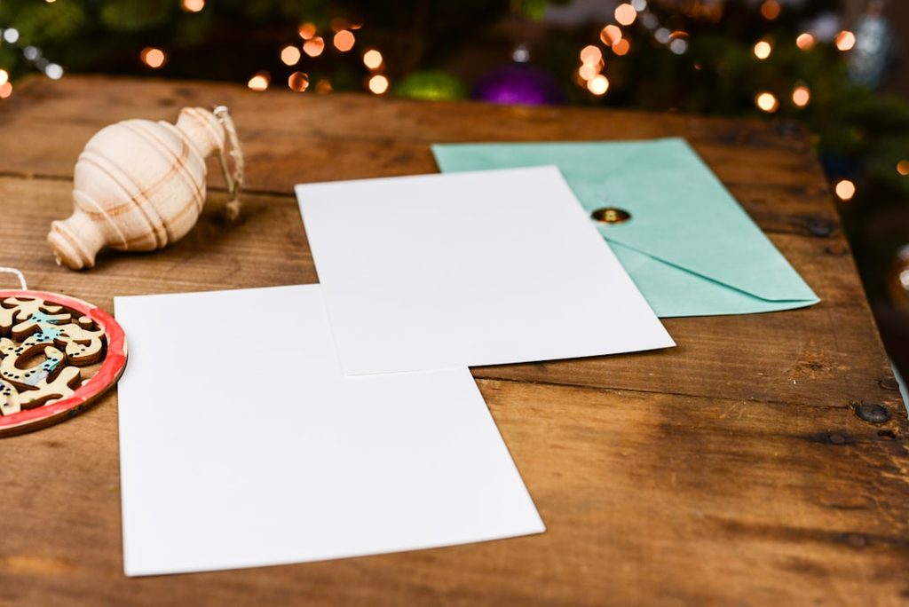 Gambar menunjukkan beberapa lembar kertas putih dan sebuah koin di atas meja kayu, dengan latar belakang lampu Natal.
