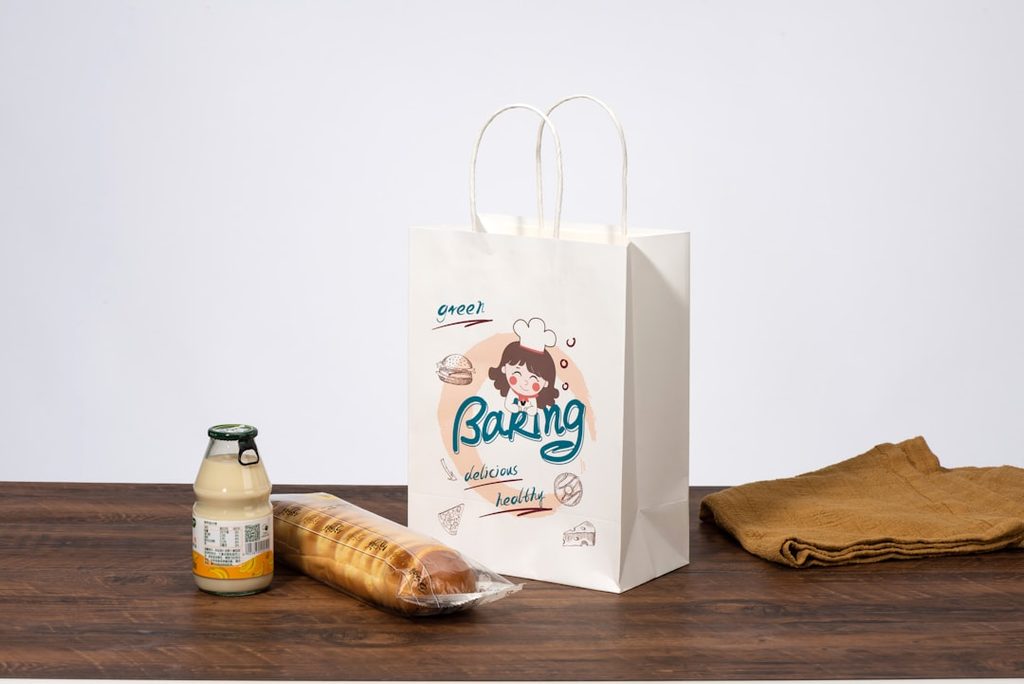 Kemasan paper bag bertuliskan 'Baking' dengan logo karakter lucu, bersama botol susu dan roti.
