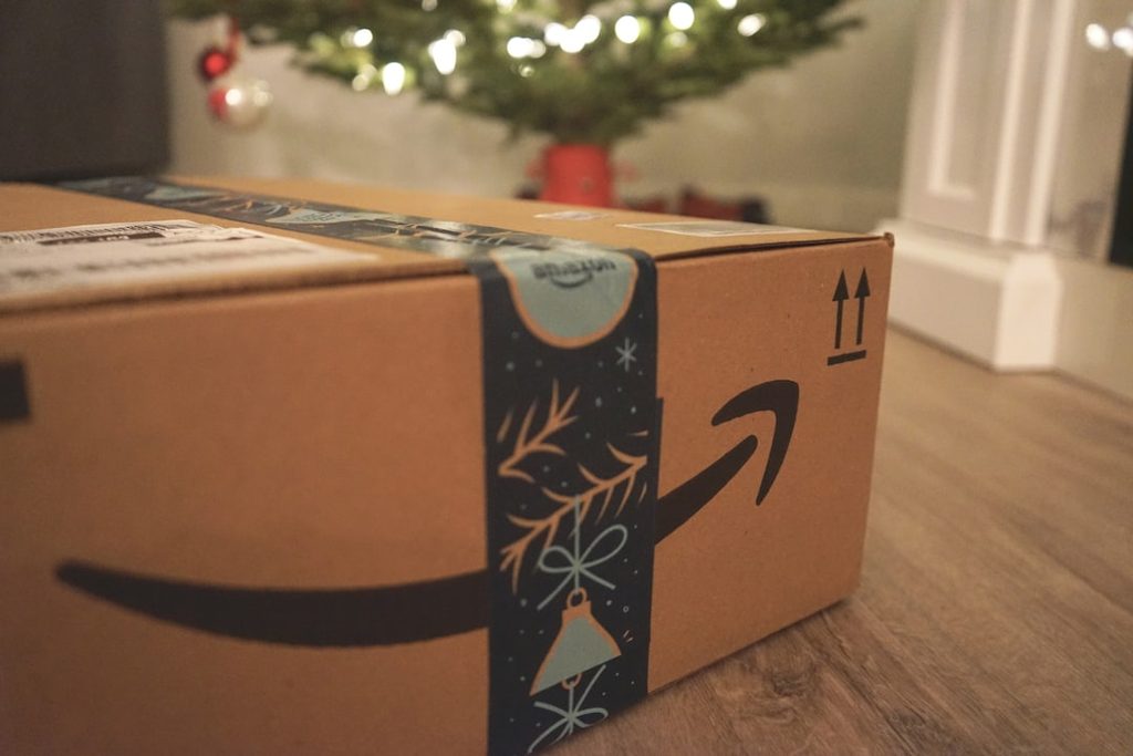 Karton Amazon dengan ikon tanda panah dan dekorasi Natal di latar belakang pohon Natal.