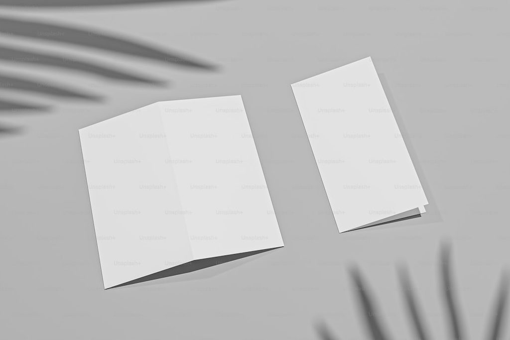 Mockup buku lipat dan kartu putih dengan latar daun.