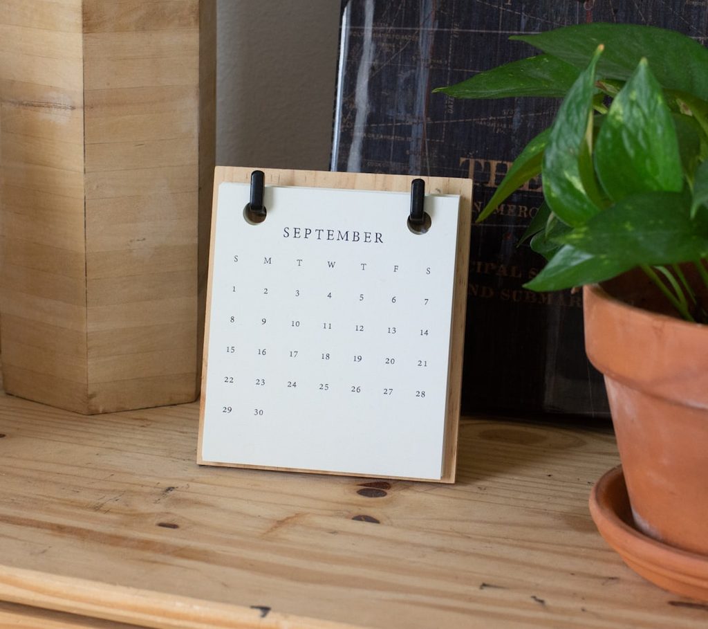 Kalender meja flip bulan September berdiri di rak kayu bersama tanaman hias, sebagai ilustrasi kalender meja yang mempercantik meja kerja.