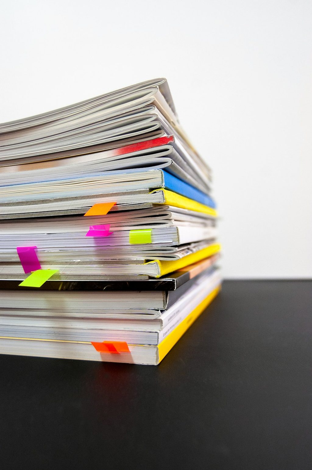 Stack of colorful booklets with sticky notes on a black surface.