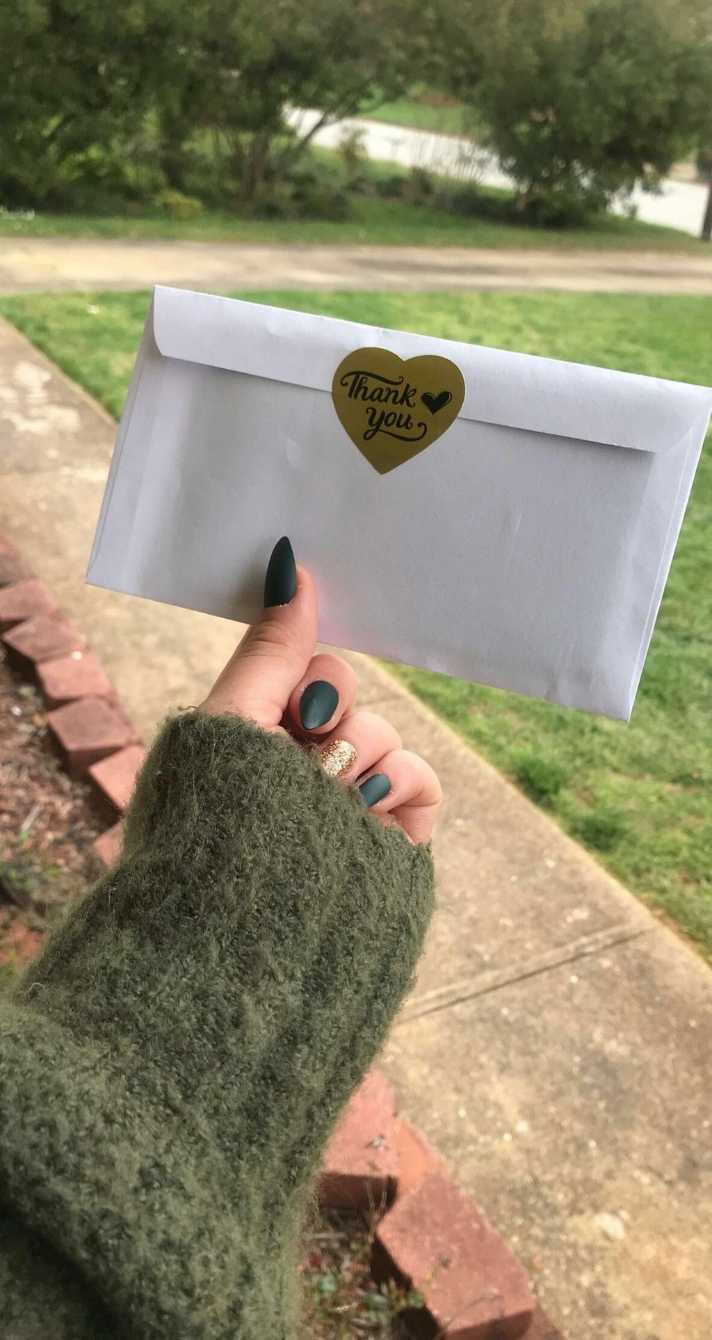 Tangan memegang sebuah envelop putih dengan stiker berbentuk hati di atasnya.