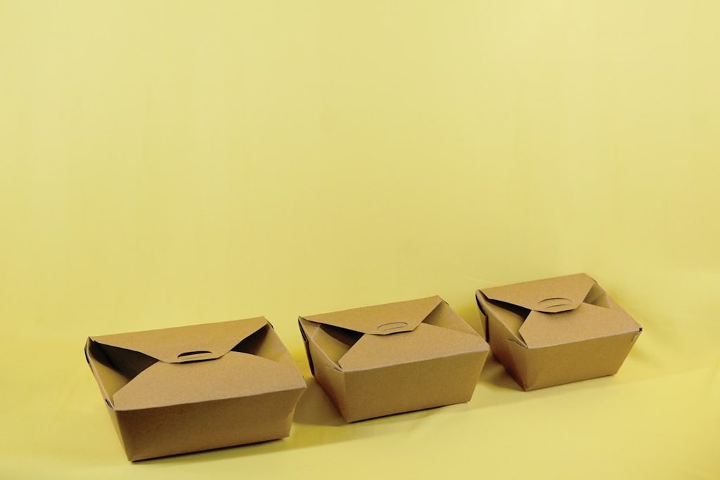 Tiga kotak makan kraft berbaris di latar kuning.
