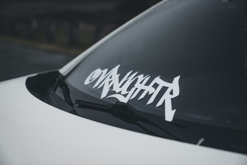 Stiker mobil pada kaca depan mobil putih sebagai contoh aplikasi outdoor yang membutuhkan bahan tahan cuaca.