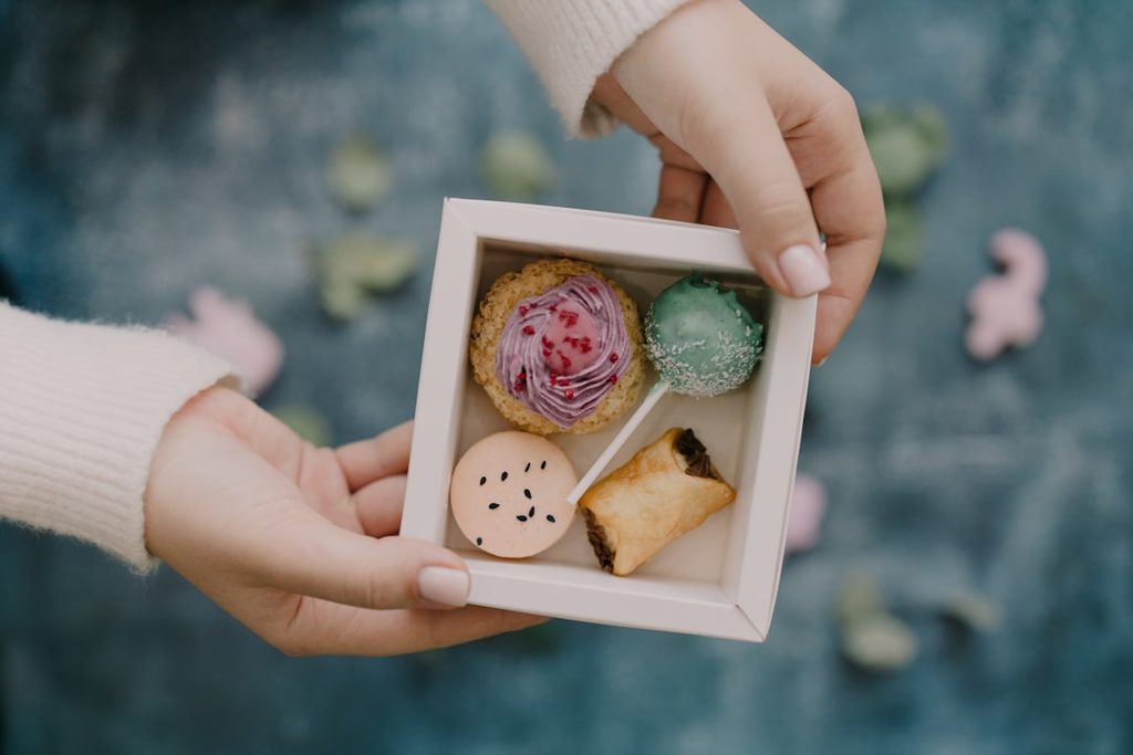 Tangan memegang kotak berisi coklat dan kue mini warna-warni.