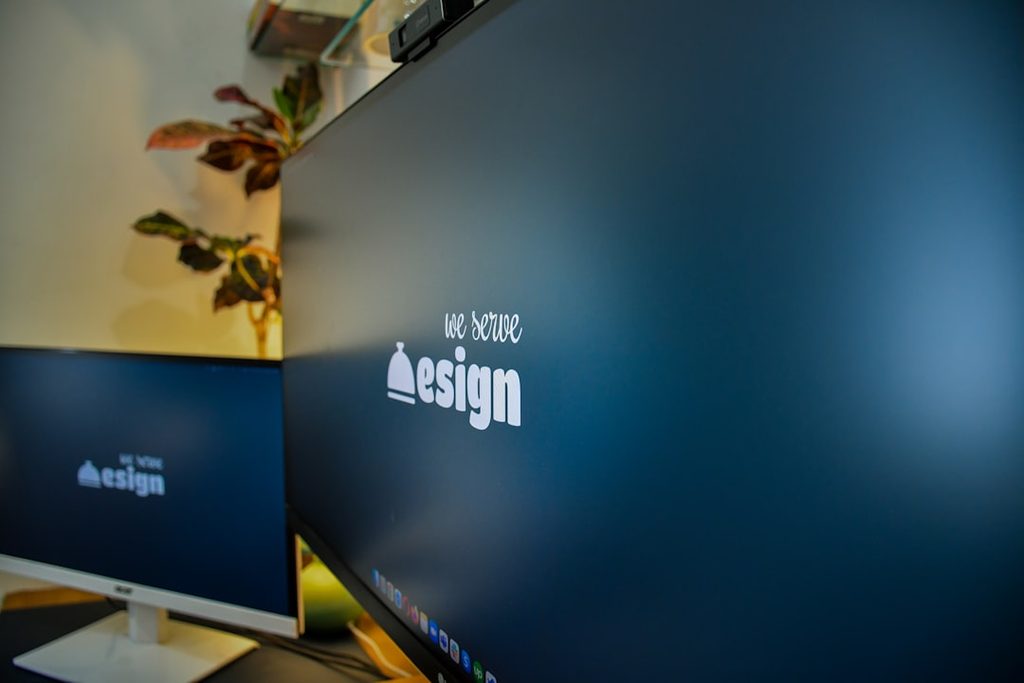 Monitor komputer dengan logo We Love Design di layar untuk menggambarkan konsistensi identitas brand pada materi cetak