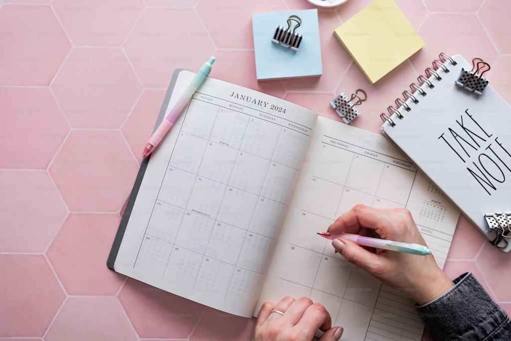 Tangan menulis di kalender percetakan online di meja pink.