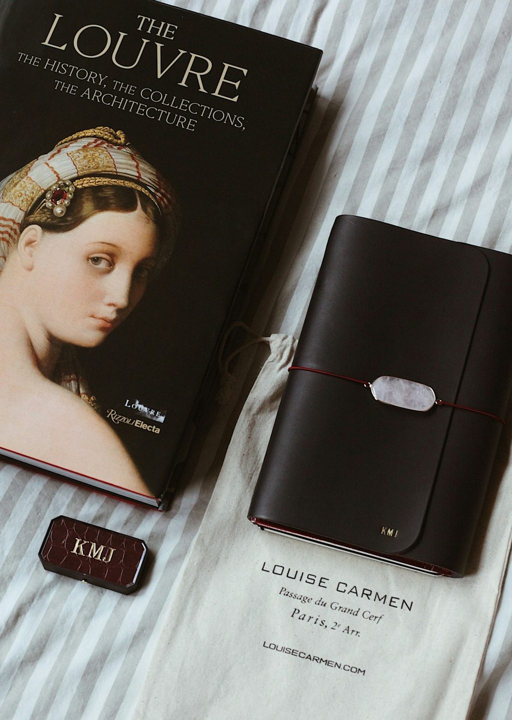 Buku 'The Louvre: The History, The Collections, The Architecture' dan agenda hitam dengan sabit putih.