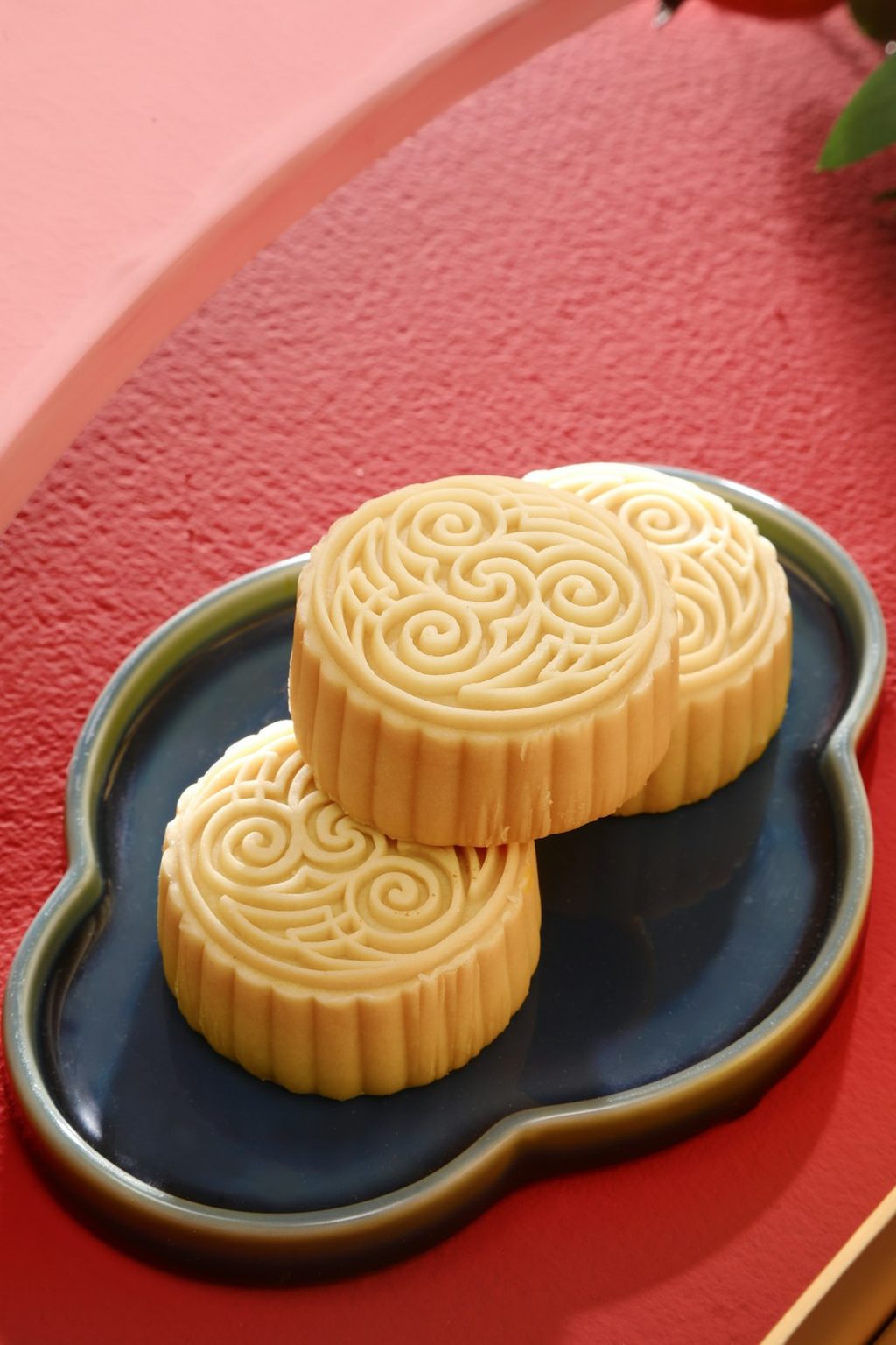 Kue bulan tradisional berbentuk bulat dengan motif spiral di atas piring berwarna gelap.