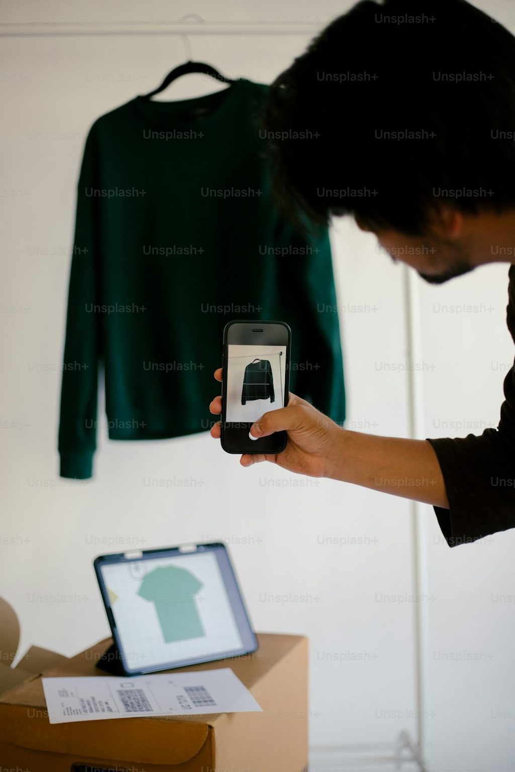 Orang memotret desain kaos di aplikasi mobile di depan kaos yang sedang dipajang.