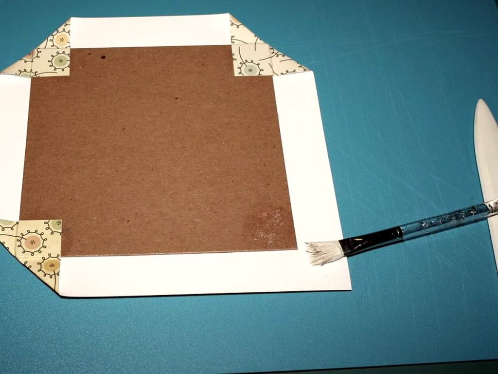 Proses pelapisan kertas luar hardbox hampers Lebaran dengan kuas lem dan alat lipat presisi.