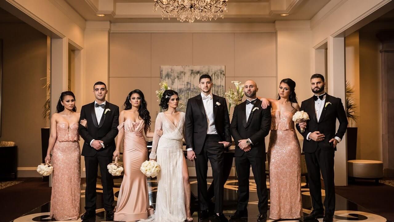 Grup pengantin dan pengiring dalam gaun formal di ruangan mewah dengan lampu kristal.