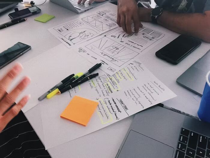 Tabel kerja dengan sketsa desain dan alat tulis di meja perkantoran.