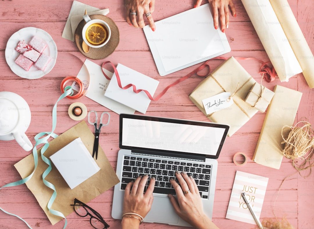 Tampilan kerja meja dengan laptop, kertas, dan bahan percetakan.