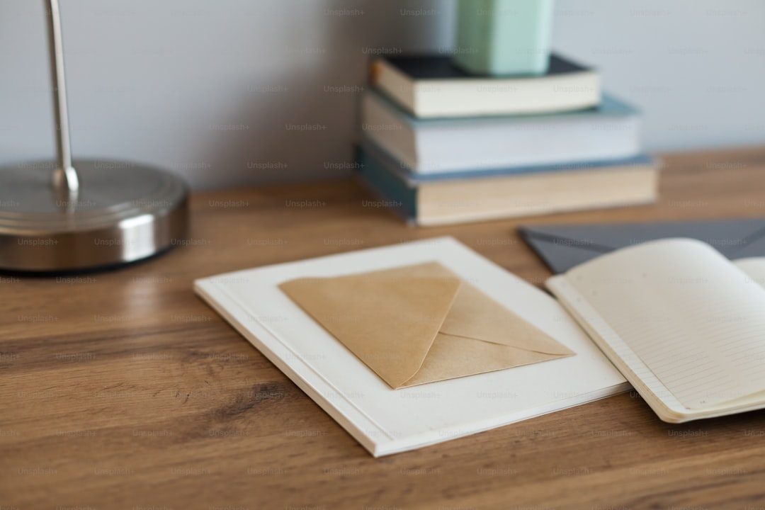 Gambar menunjukkan percetakan online dengan envelope dan buku terbuka di meja kayu.