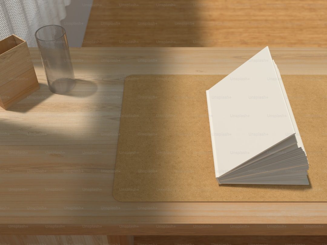 Stack of blank paper on a wooden desk with a glass and box in the background.