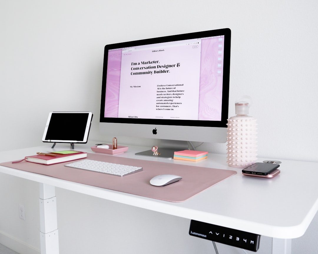 Meja kerja minimalis dengan monitor iMac, mouse, dan peralatan pekerjaan.