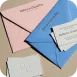 Amplop kertas pastel dengan sisipan putih di atas permukaan datar.