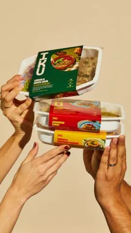 Wadah makanan plastik dengan label cetak berwarna yang dipegang beberapa tangan.