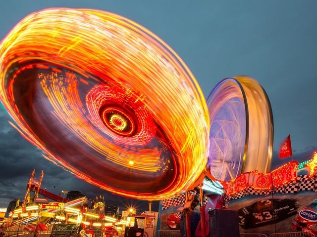 Gambar permainan berputar dengan cahaya neon dan gerbang pameran di malam hari.