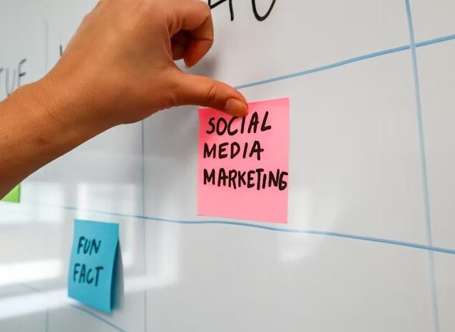 Tangan menempelkan stiker merah 'SOCIAL MEDIA MARKETING' di papan tulis.