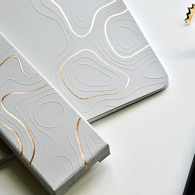 Buku hardcover putih dengan desain topografi emas, cocok untuk promosi branding.