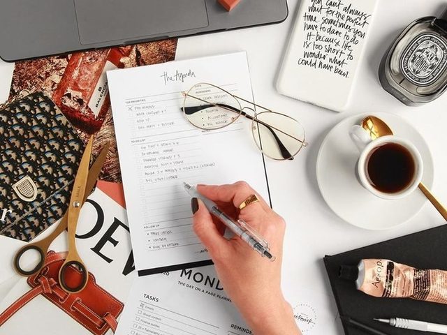 Tulis agenda harian dengan laptop dan alat kerja di meja kerja.
