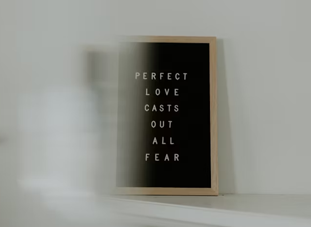 Gambar poster hitam dengan tulisan 'Perfect Love Casts Out All Fear' di dinding putih.