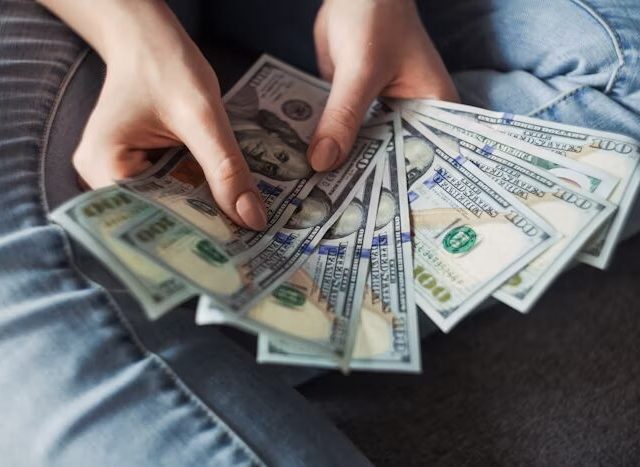 Tangan memegang beberapa lembar uang dolar AS, menunjukkan konsep keuangan atau pembayaran.