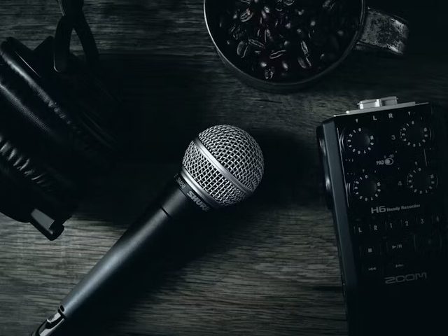 Microphone, audio recorder, and coffee beans on a wooden surface sebagai ilustrasi perlengkapan meja kerja dan area display promosi