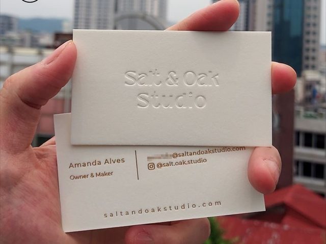 Tangan memegang kartu nama putih dengan logo dan detail kontak 'Salt & Oak Studio'.