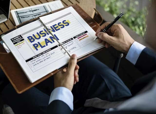 Tangan menulis pada lembaran bisnis plan di Uprint.id saat menyiapkan konsep booklet landscape A5 untuk kebutuhan bisnis
