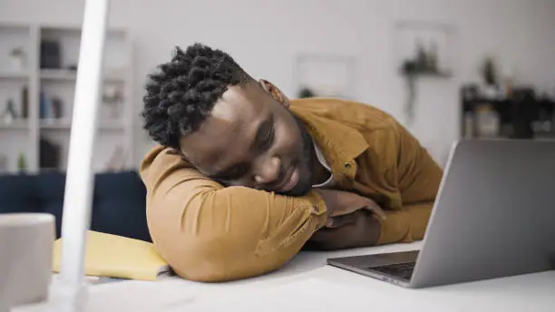 Pria tidur santai di meja dengan laptop dan lampu di depannya.