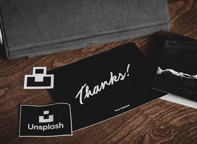 Gambar menunjukkan kartu ucapan 'Thanks!' dari Unsplash dan logo Uprint.id di atas meja kayu.