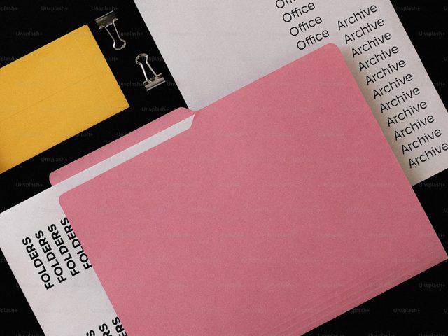 Gambar menunjukkan folder archive berwarna merah muda dan lembaran kertas putih dengan tulisan 'Archive' di bagian atas.