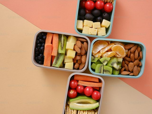 Lunchbox berisi berbagai makanan sehat, termasuk buah-buahan, sayuran, dan kacang-kacangan.