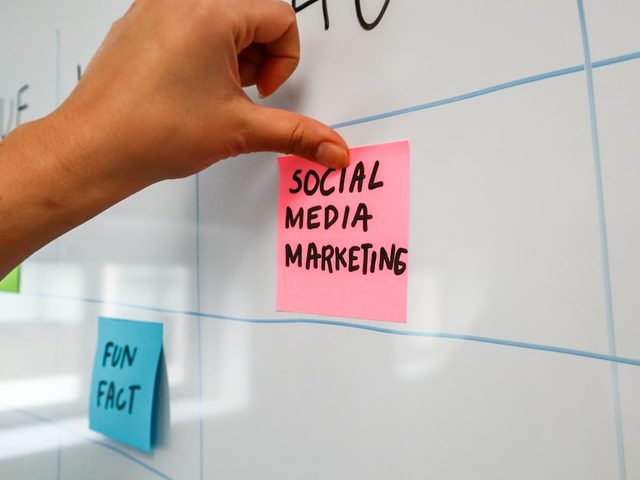 Tangan menempelkan stiker merah dengan tulisan 'SOCIAL MEDIA MARKETING' di whiteboard.