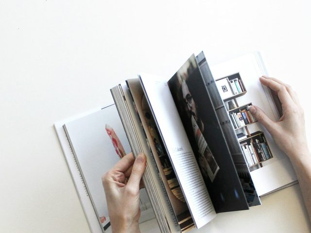 Tangan memegang buku dengan desain grafis modern di halaman putih.
