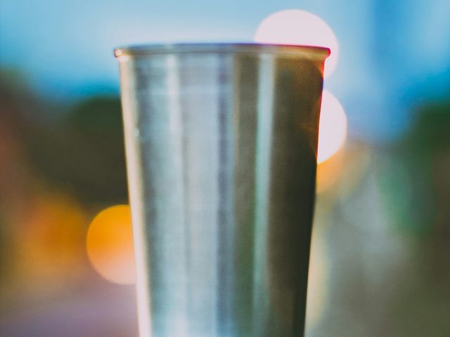 Gelas stainless modern dengan cahaya bokeh di latar belakang.