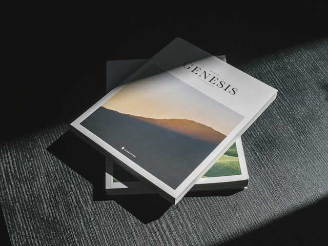 Buku Genesis dengan cover berwarna biru dan hijau, diletakkan di atas meja.